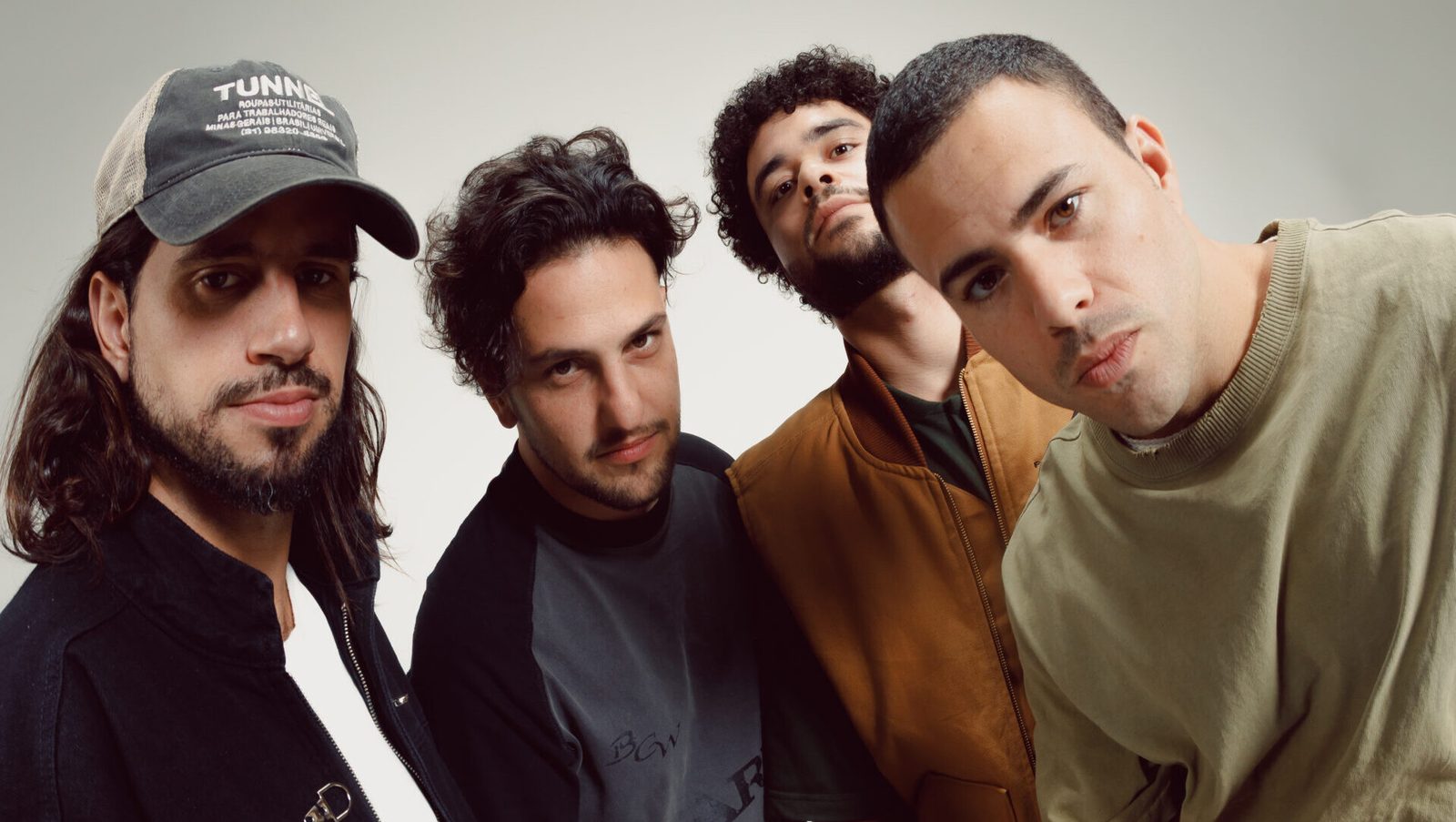 Os quatro integrantes do Lagum lado a lado, olhando para a câmera, em foto de estúdio