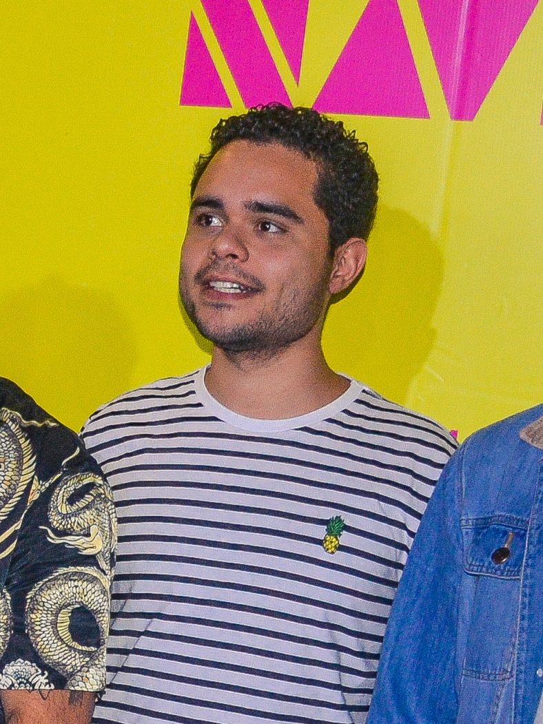 Jorge sorrindo, de colete caramelo sobre camiseta verde
